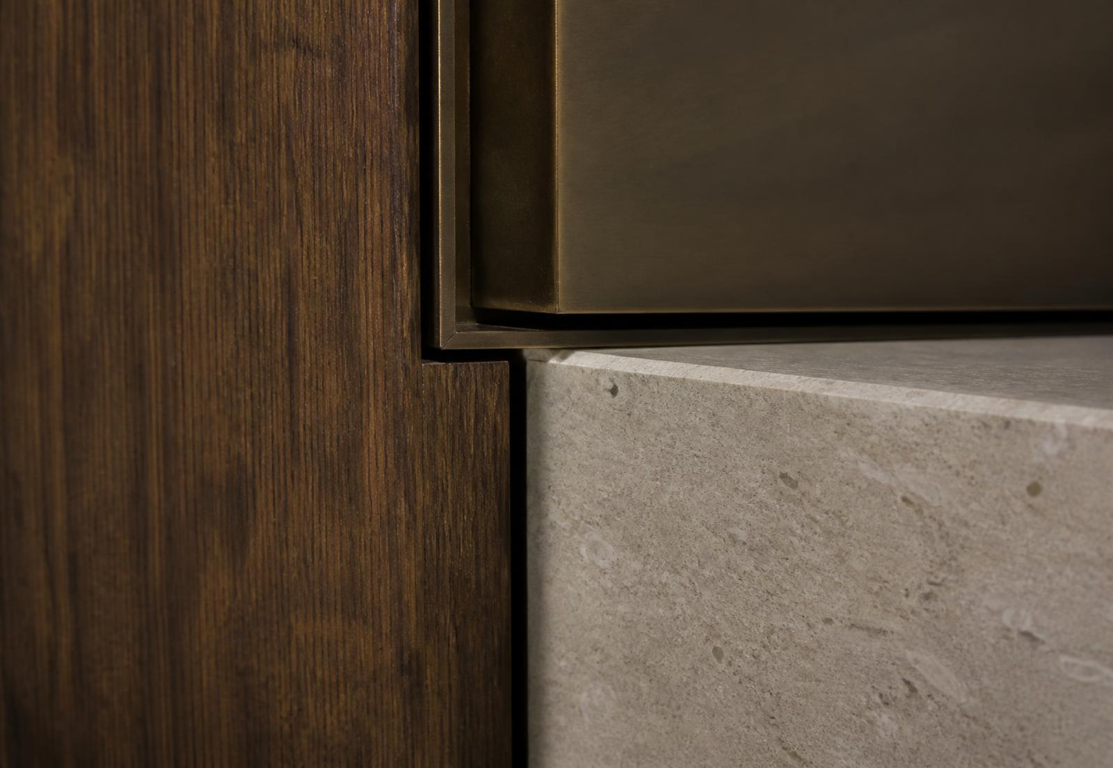 Close detail of walnut veneer meeting a bronze reveal and honed limestone